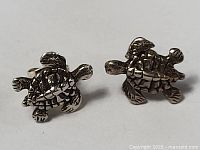 Front view of two sterling silver turtle-shaped stud earrings on white background.