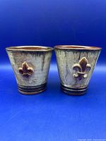 Front view of both mugs showing fleur-de-lis motif and glaze coloring