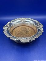 Angled view of silver-plate wine coaster showing ornate border and wood base