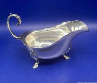 Profile view of sterling silver sauce boat showing scalloped rim, scroll handle and three feet