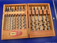 Open wooden case displaying 13 auger bits in size order