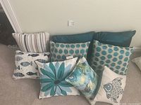 Nine assorted decorative throw pillows arranged on floor showing patterns and colors.