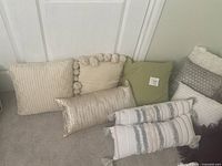 Group of 10 pillows arranged on floor near wall, showing variety of textures and shapes