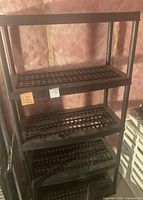 Front view of black plastic shelving unit with five ventilated shelves showing the grid pattern and support poles.