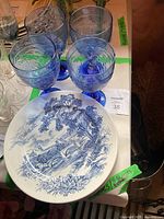 View of 4 blue stemmed glasses and 1 ceramic plate with blue and white scenic design