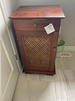 Front view of wood cabinet showing top drawer and rattan inset door with brass pulls