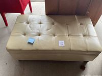 Top view of cream-colored real leather ottoman showing tufted design and creasing.