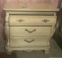 Front view of ivory dresser showing three drawers with detailed ornate handles and carved wood accents.