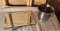 Photo showing the rectangular mirrored glass serving tray with geometric lattice design beside the stainless steel ice bucket on a beige surface.