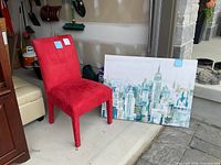 Red suede accent chair next to cityscape artwork leaning against the wall in a garage.