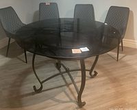 Full view of round glass top dining table with metal frame and 4 diamond quilt patterned chairs arranged around it, showing the table shape, leg design, and chair style.
