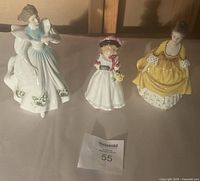 Set of three Royal Doulton porcelain Victorian-era women figurines displayed on a white cloth under warm light.