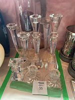 Shows 12 clear crystal candle holders of varying shapes and sizes, including tall taper holders and shorter votive holders in crystal material.