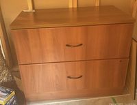 Closed view of the entire medium brown wooden filing cabinet with two drawers and black handles.