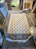 Full view of the rug laid on a carpet floor showing the overall floral design with cream center and blue floral border, white fringe on edges.