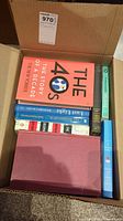 Box containing a collection of various books seen stacked and lying flat, showing titles including 'The 40: The Story of a Decade'.