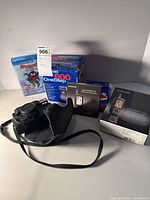 Lot contents including Minolta camera in case, Polaroid 600 OneStep in box, Garmin GPS units in boxes, and Spider-Man DVD.