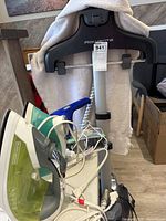 Rowenta standing clothes steamer with hanger, Black & Decker handheld vacuum, and irons grouped together on floor near a chair