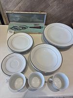 Full view of the collection showing stacked ceramic dishes including plates, bowls, saucers, and teacups, alongside a boxed set of serving cutting utensils.