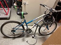 Full side view of the Dunlop bicycle showing blue and white frame, wheels, handlebars, seat with green tape, helmet on handlebar, and floor pump on ground.