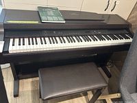 Full frontal image of Yamaha Clavinova electric piano with padded bench and owner's manual on top, showing keyboard and part of the control panel.