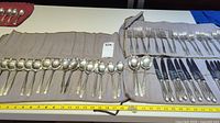 Full set of silverware including knives, forks, and spoons laid out on cloth rolls with measuring tape alongside.