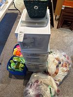 Overview of plastic drawer unit with clear bins on top, woven basket, fabric bins and plastic bags of quilt tops