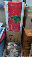 Image of boxed 7.5 ft faux Christmas tree alongside two decorative Christmas cushions with winter house scene.