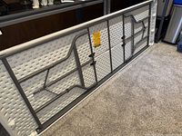 Bottom side of the folding table showing white textured plastic top and folded gray metal legs and support bars.