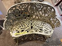 Front view of the white cast iron garden bench with ornate scrollwork design and peeling paint.