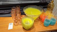 Set of assorted glassware on wooden surface including amber-colored stem glasses, large yellow bowl, smaller yellow bowls, and frosted blue and orange glasses