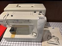 Full view of white Kenmore sewing machine with carrying case behind it, showing controls and model sticker.