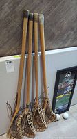Five wooden lacrosse sticks leaning against wall