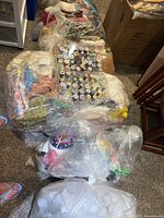 Overview of six sealed plastic bags of fabrics and two clear thread bins on carpeted floor