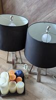 Pair of lamps with black shades and metal tripod bases shown with assorted candles on tray.