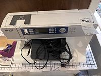 Front view of Pfaff sewing machine with power cord and foot pedal on grid background