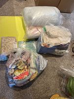 Photo shows two large plastic bags: one containing a large roll of cotton batting, one with assorted fabric pieces, placed on a yellow cutting mat with grid lines.