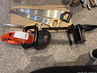 Overview of all three saws: two wooden handle handsaws, one compact orange Mastercraft chainsaw, and a Black & Decker tree trimmer.