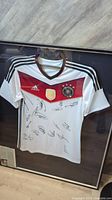 Front view of framed signed Germany national team jersey with multiple autographs visible