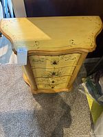 Front view showing the entire small painted cabinet with floral design on drawers and yellow painted surface.