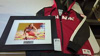 Photo showing the framed signed photograph and the red and black Canada track and field jacket.