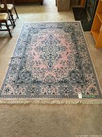 Full view of rectangular area rug laid out on floor showing traditional floral medallion pattern with pink center field and blue cream decorative border and cream fringes on the ends.