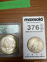 1921 Morgan dollar in slab beside loose 1925 Peace dollar front view