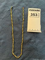 Full view of gold figaro chain alongside lot card
