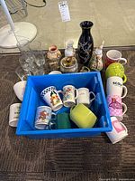 Full lot view showing mugs in blue tote, multiple vases, drinking glasses
