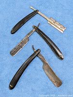 Group of four straight razors and one safety razor head on blue cloth