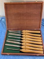 Open wooden case showing eight chisels on green felt
