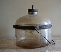 Side view showing full glass container, metal band, bail handle and cap