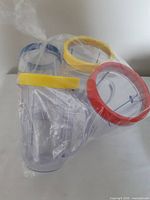Three clear Magic Bullet cups in plastic bag showing blue, yellow and red rims