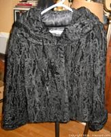 Front view of black sheared Persian lamb fur jacket on hanger showing texture and collar